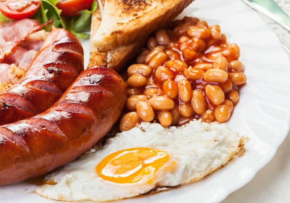 Full English breakfast with bacon, sausage, fried egg, baked beans and tomato salad