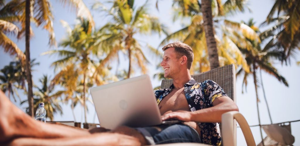 digital nomad in a tropical location working from laptop with palm trees in background